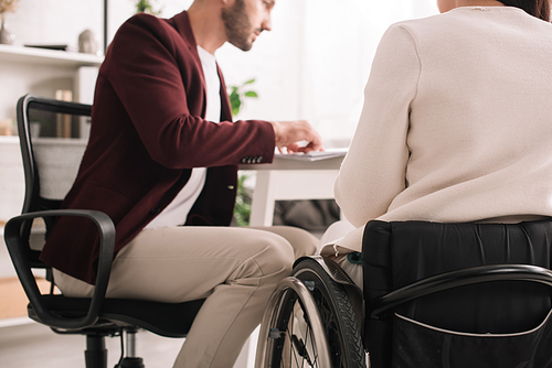 cropped view of disabled businesswoman sitting at desk near colleague