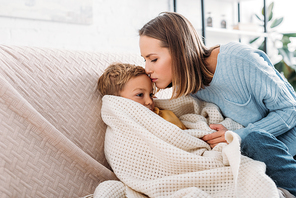 caring mother kissing diseased son wrapped in blanket
