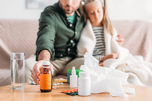 selective focus of father taking cough syrup while sitting near diseased daughter