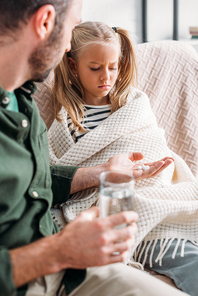selective focus of man giving pills to upset, diseased daughter