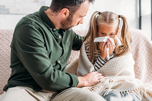 attentive father embracing sick daughter sneezing in napkin