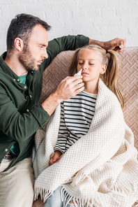 attentive father holding nasal spray near sick, upset daughter