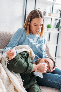 attentive wife holding thermometer near diseased husband sneezing while lying on her laps