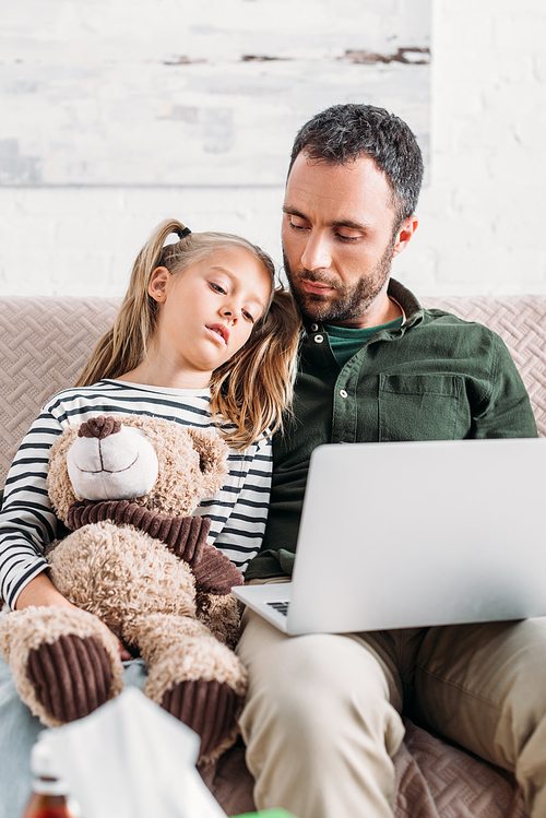 diseased kid using laptop with father while sitting on sofa