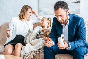 worried father holding medicines and mother sitting near diseased daughter