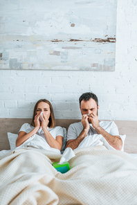 diseased husband and wife sneezing while lying in bed together