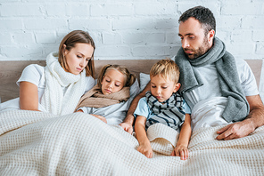 sick family in warm scarfs lying in bed under blankets