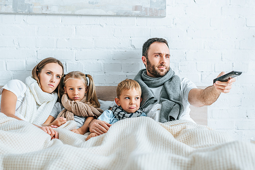 sick family lying in bed and watching tv together