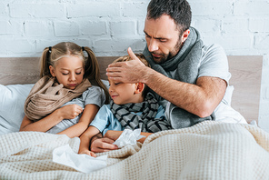 worried man touch forehead of diseased son while lying in bed together