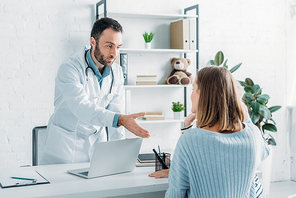 smiling doctor outstretching hand to woman sitting at desk