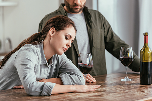Disappointed woman holding wine glass beside husband