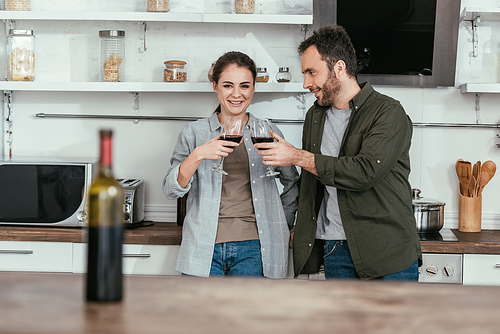 Selective focus of smiling couple toasting with red wine on kitchen