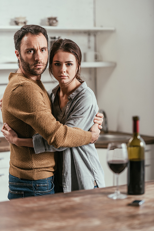 Selective focus of man hugging alcohol dependent wife in kitchen