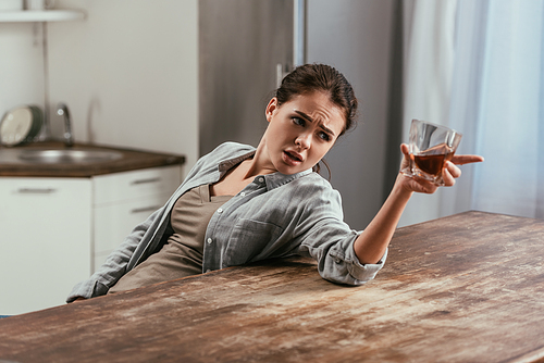 Angry woman with whiskey glass talking to somewhere at kitchen table