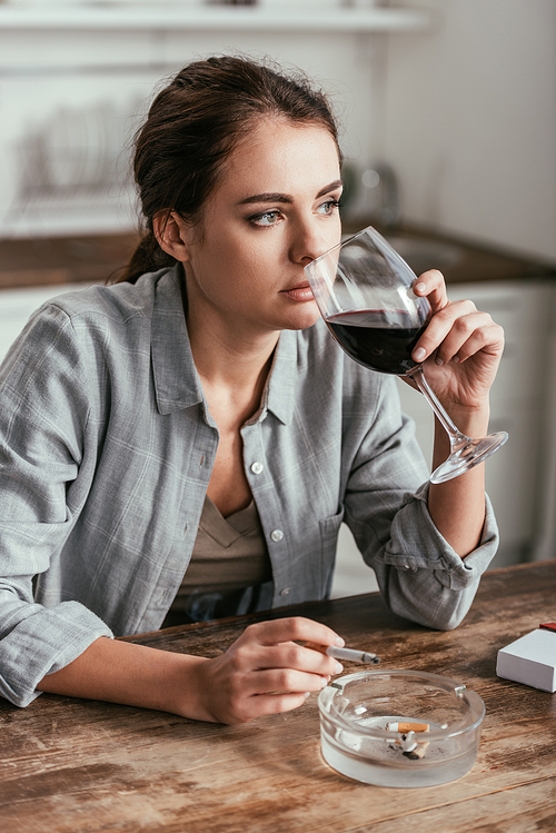 Pensive woman drinking wine and smoking at kitchen table