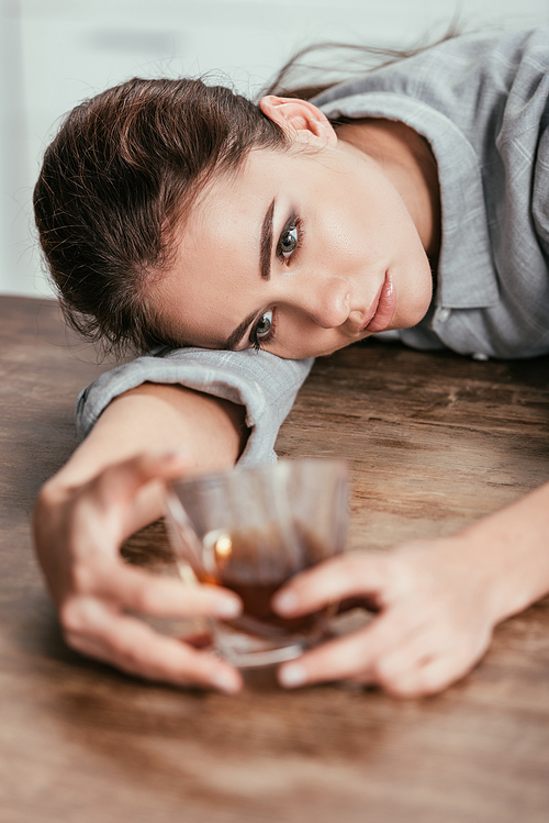 Selective focus of upset woman looking at whiskey glass at table