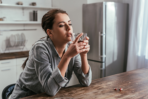 Depressed woman holding whiskey glass beside pills on table