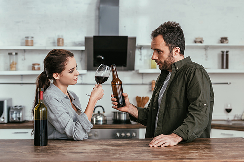 Couple with wine and beer clinking at kitchen