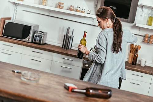 Selective focus of woman holding wine bottle and cigarettes with beer on kitchen table