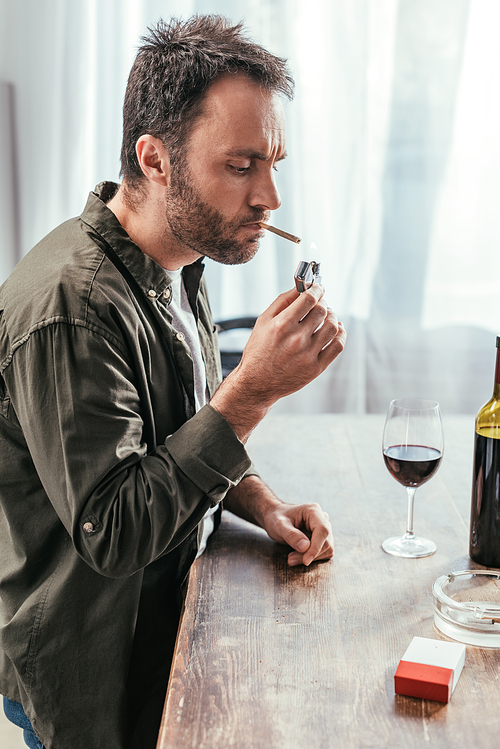Man lighting cigarette beside wine bottle and glass on table