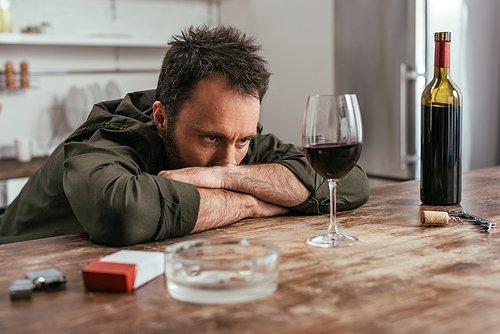 Disappointed man looking at wine glass beside cigarettes on table