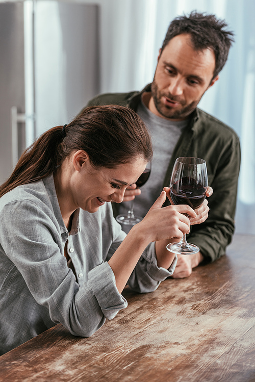 Selective focus of couple with wine glasses laughing on kitchen