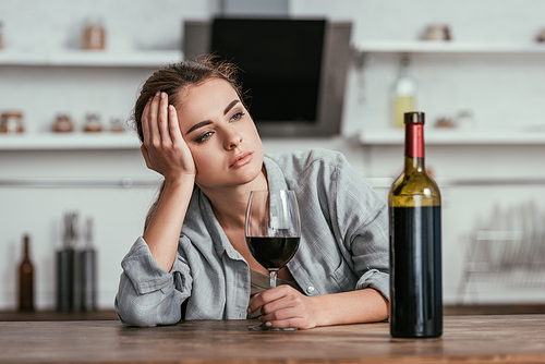 Disappointed woman holding wine glass on kitchen table