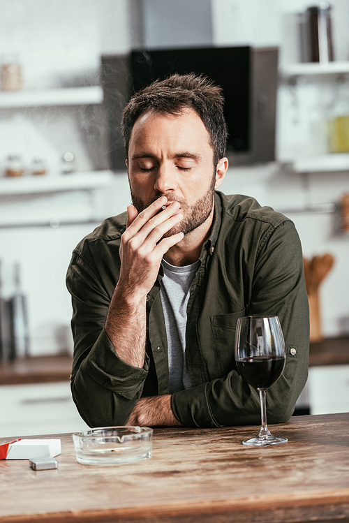 Man smoking cigarette beside wine glass on kitchen table