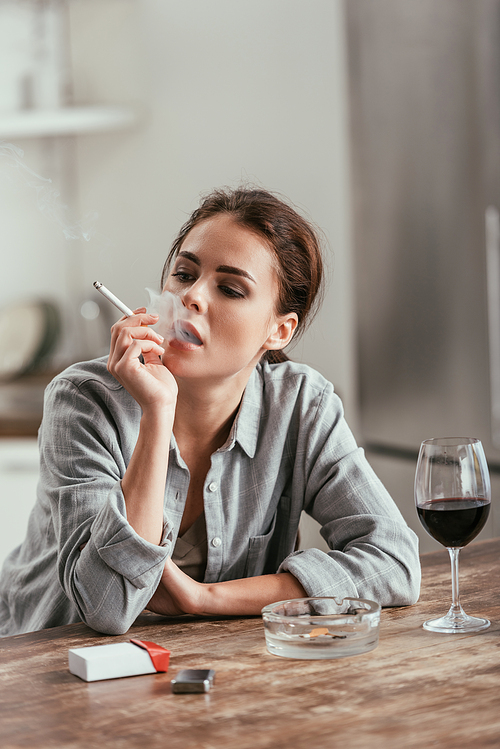 Woman smoking cigarette beside wine glass on table