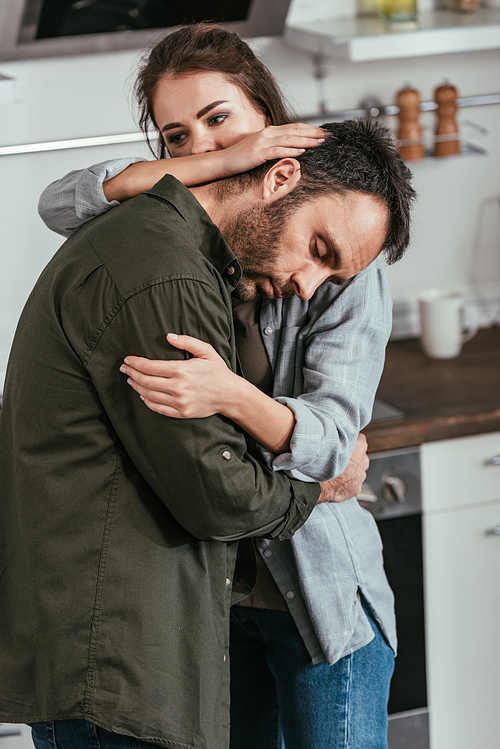 Woman hugging worried husband with alcohol addiction on kitchen