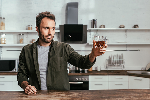 Man with whiskey glass toasting to someone on kitchen