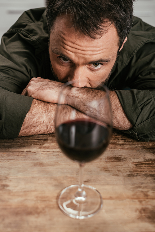 Selective focus of alcohol addicted man looking at wine glass on table