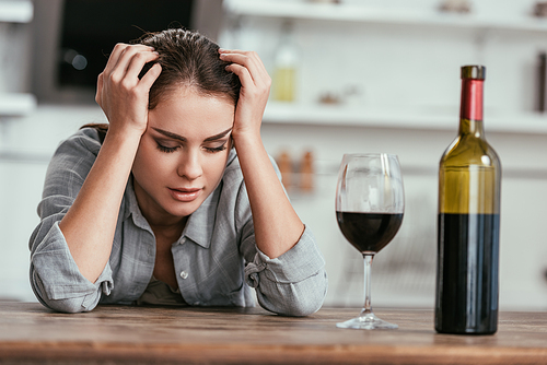 Selective focus of woman with alcohol addiction sitting beside wine on kitchen table