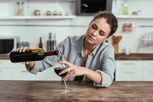 Upset woman pouring wine in glass at kitchen table
