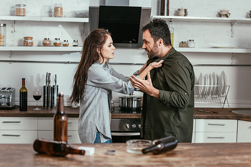 Selective focus of angry woman quarreling with alcohol addicted husband on kitchen