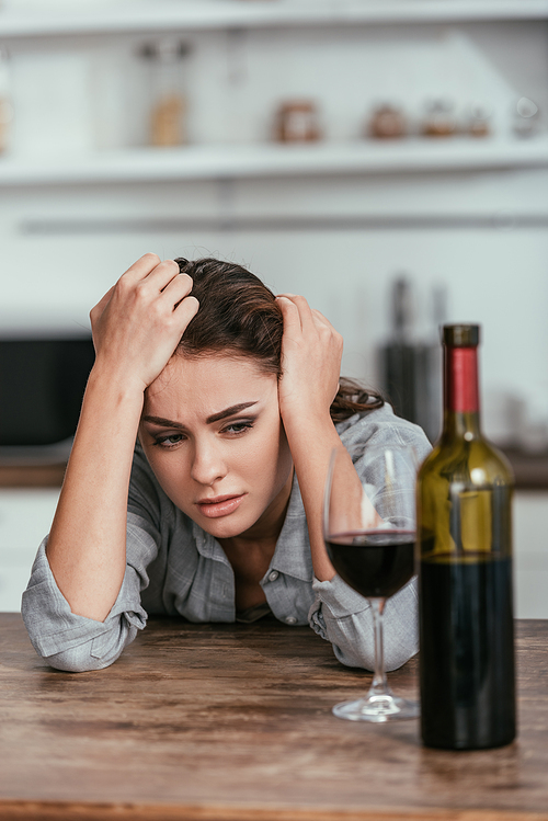 Selective focus of depressed woman looking at wine on table