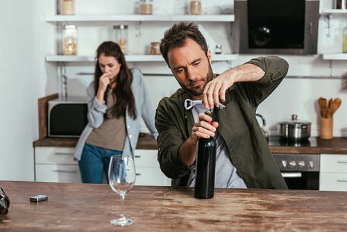 Selective focus of man opening wine bottle and worried wife on kitchen