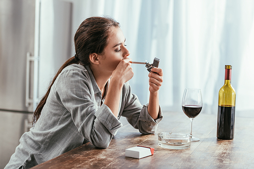 Woman smoking cigarette with wine on kitchen table