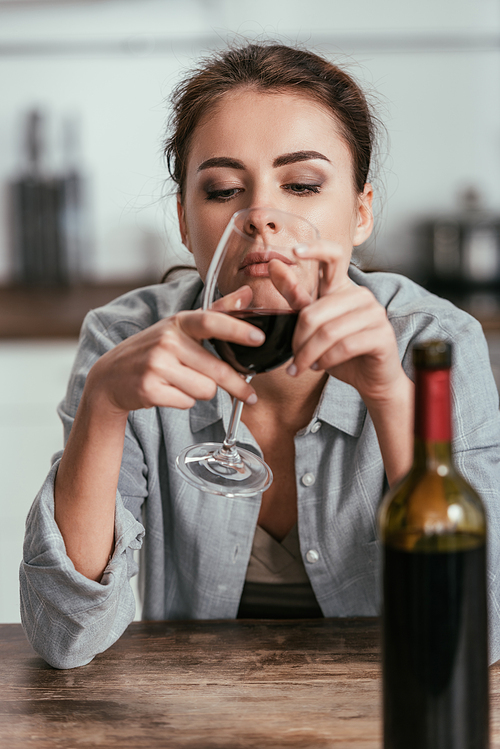 Selective focus of sad woman looking on wine glass