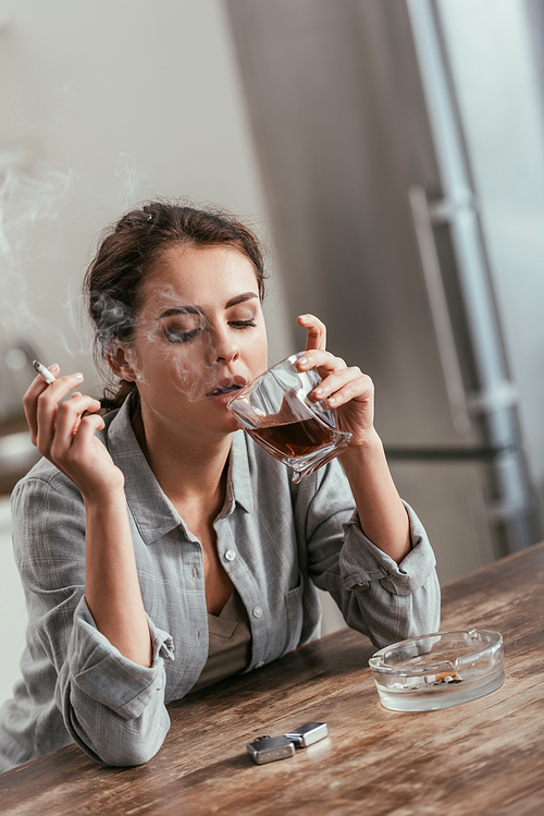 Woman smoking cigarette and holding whiskey glass at table