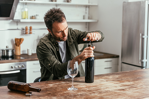 Alcohol addicted man opening wine bottle on kitchen