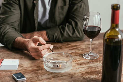 Cropped view of man smoking cigarette beside wine glass on table