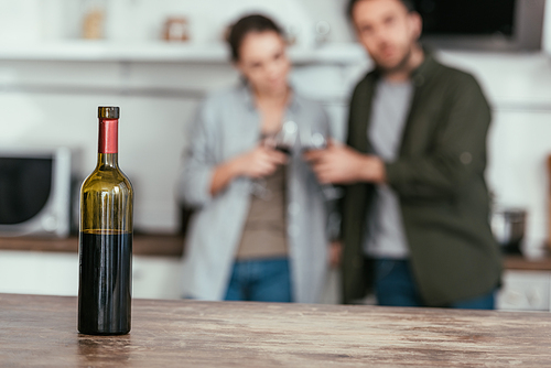 Selective focus of wine bottle on table and couple with glasses at home