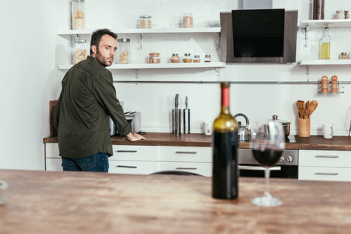 Selective focus of pensive man looking at wine on kitchen table