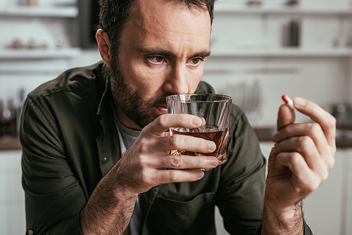 Selective focus of man with alcohol depended holding whiskey glass and pill