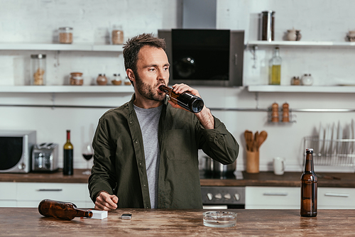 Man with alcohol depended drinking beer at kitchen