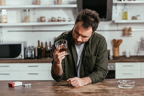 Worried man with alcohol depended holding whiskey glass at kitchen