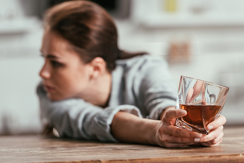 Selective focus of sad woman holding whiskey glass at table