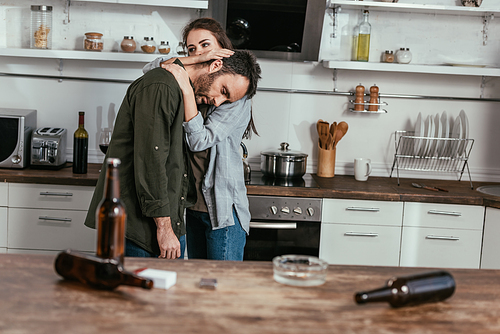 Selective focus of woman calming down worried husband with alcohol addiction at kitchen