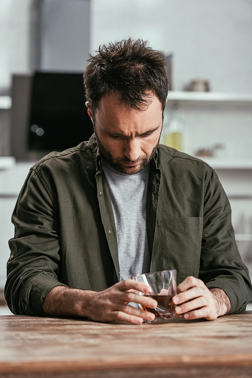 Worried man holding whiskey glass at kitchen table